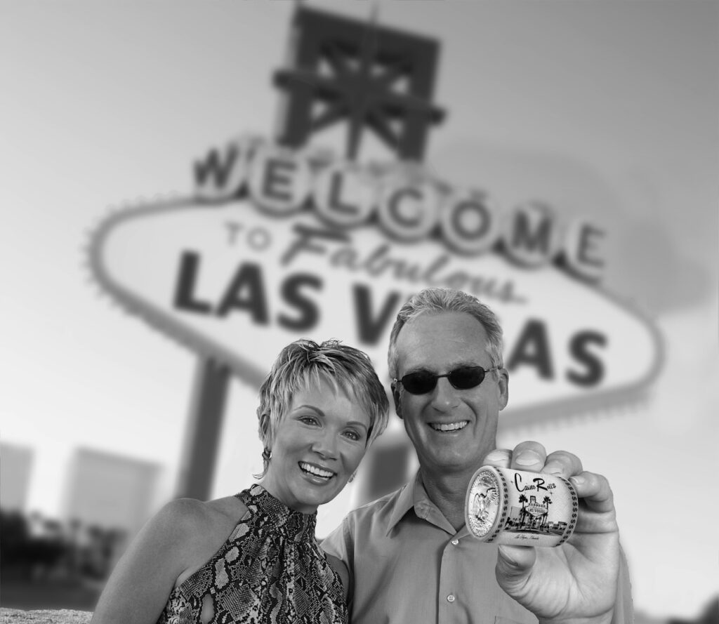 Smiling couple holding a Casino Roll, standing in front of the "Welcome to Fabulous Las Vegas" sign.